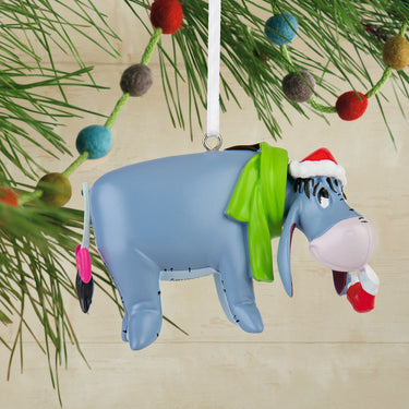Christmas ornament of Eeyore with a Santa hat hanging on a tree branch.