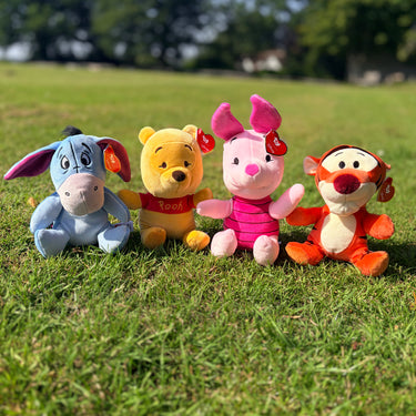 Four Winnie the Pooh plush toys on grass with a blurred background