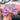 Pink bow tie with heart and balloon pattern held by a hand, against a colorful background.