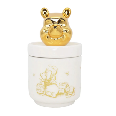 A white porcelain collector's pot with a gold-colored Winnie the Pooh bear figurine on top.