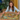 Woman working on a colorful puzzle at a table with plants and curtains in the background