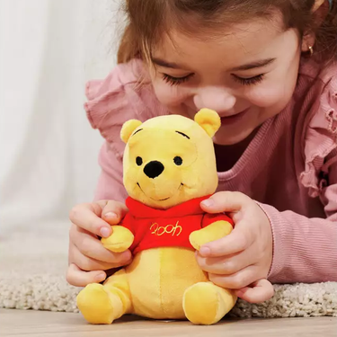Child holding a small Winnie the Pooh plush toy with a red shirt.