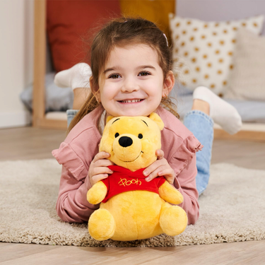 Child holding a plush Winnie the Pooh toy on a carpeted floor.